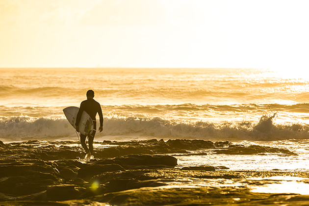 A surfer entering the water with his board at sunrise